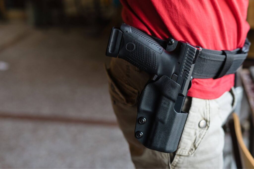 Man in a red shirt wearing an outside the waistband holster with a firearm safely stored