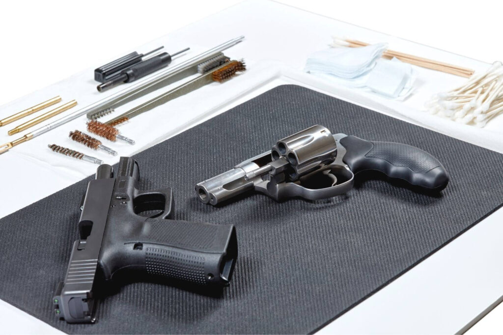 Two firearms placed on a black mat with gun cleaning accessories surrounding them