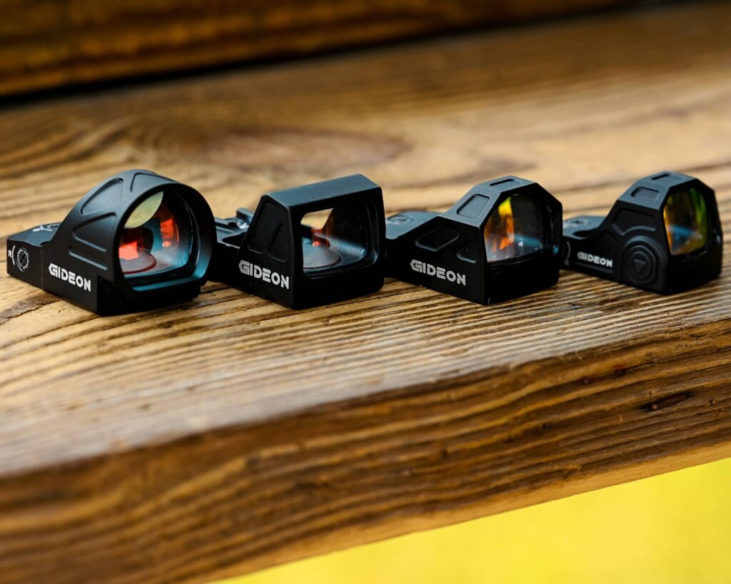 Various gideon optics red dot sights sitting on a wooden table