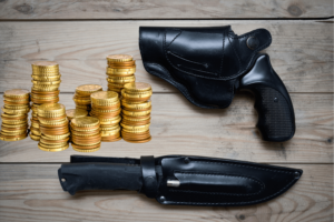 Gun, knife, and gold coins laid out on a wood table