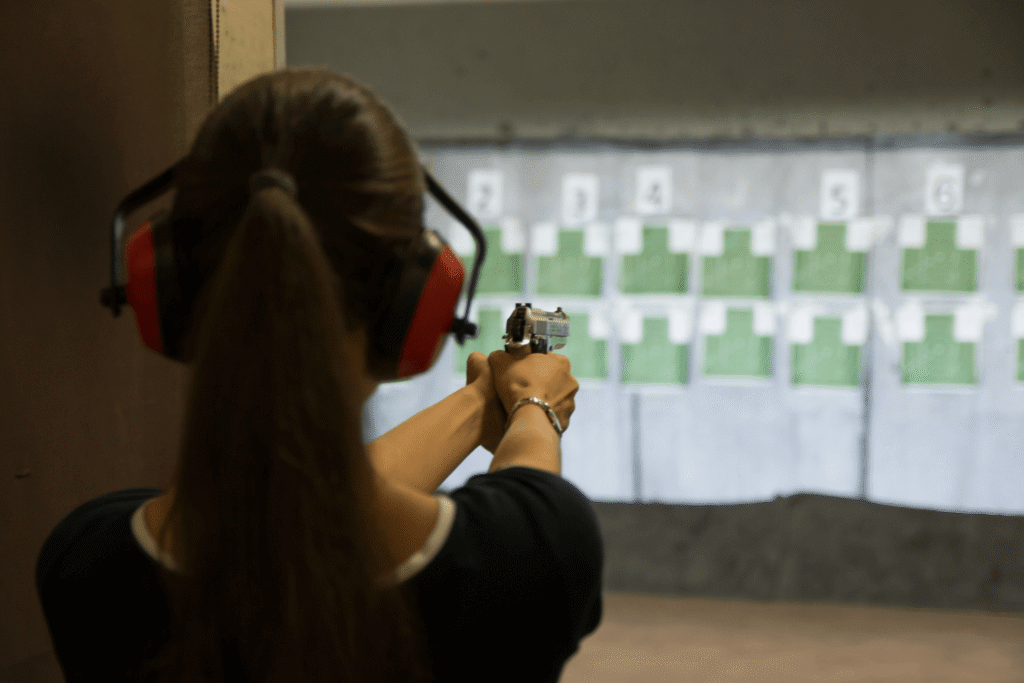 behind the back view of a woman aiming her pistol at a target at an indoor shooting range