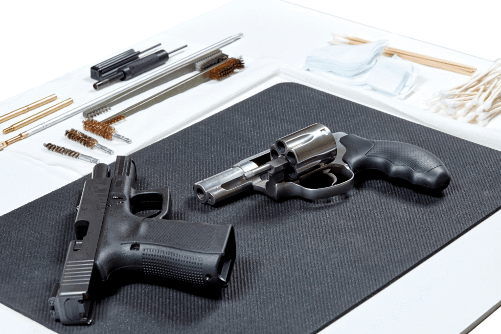 gun cleaning kit surrounding two pistols that are laid out on a black mat