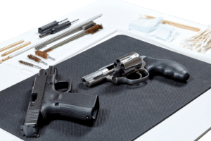 gun cleaning kit surrounding two pistols that are laid out on a black mat