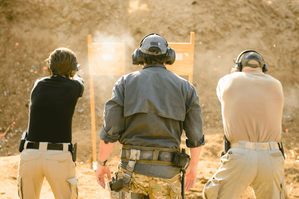 behind the back view of two men firing weapons as an instructor watches at an outdoor shooting range