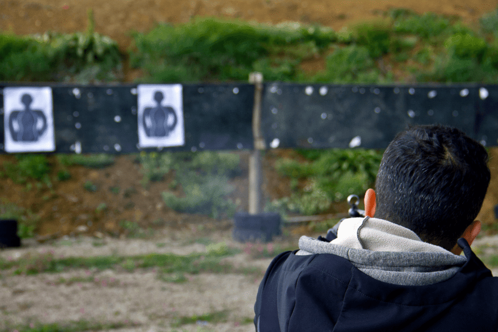 behind the back view of a man firing his gun at an outdoor shooting range