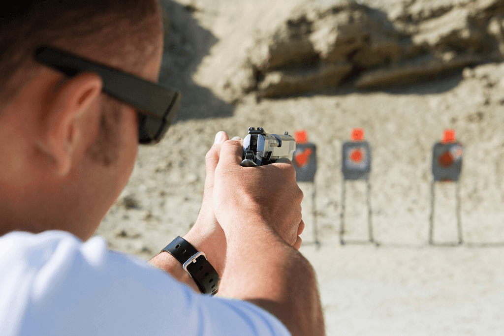 behind the back view of a man aiming his pistol at a target at an outdoor shooting range